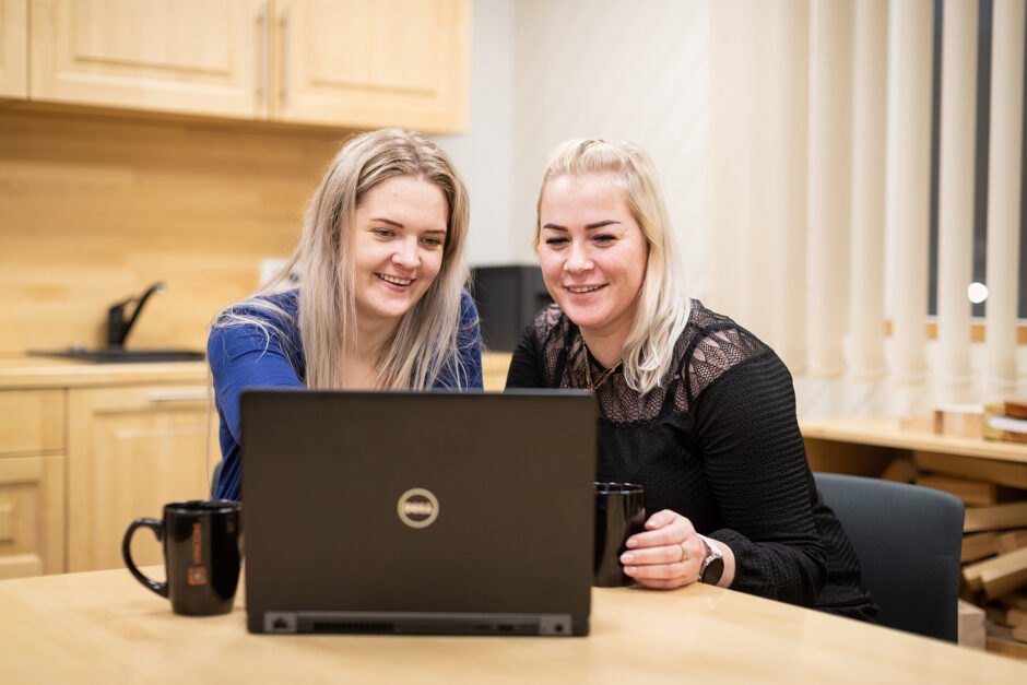 Two women in an office kitchen behind a laptop